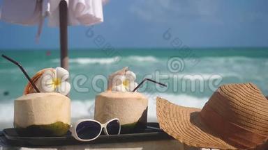 热带新鲜的椰子鸡尾酒，在带绿松石海的海滩咖啡馆里，装饰着弗兰吉帕尼的花朵和带帽子的太阳镜